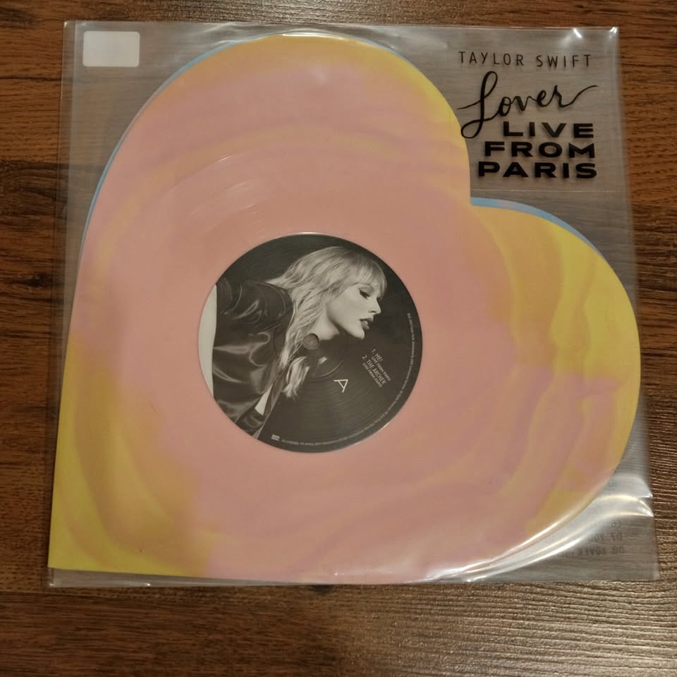 Vinyl record in packaging with Taylor Swift's face on a pink and yellow background
